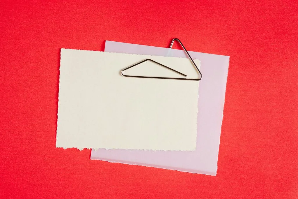 Two separate pieces of paper joined by a single paperclip against a red background, evoking the idea of linking distinct repositories together.