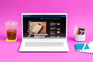 The Asus Chromebook Plus CX34 displaying The Verge homepage between an iced coffee and a cup of colored pencils.